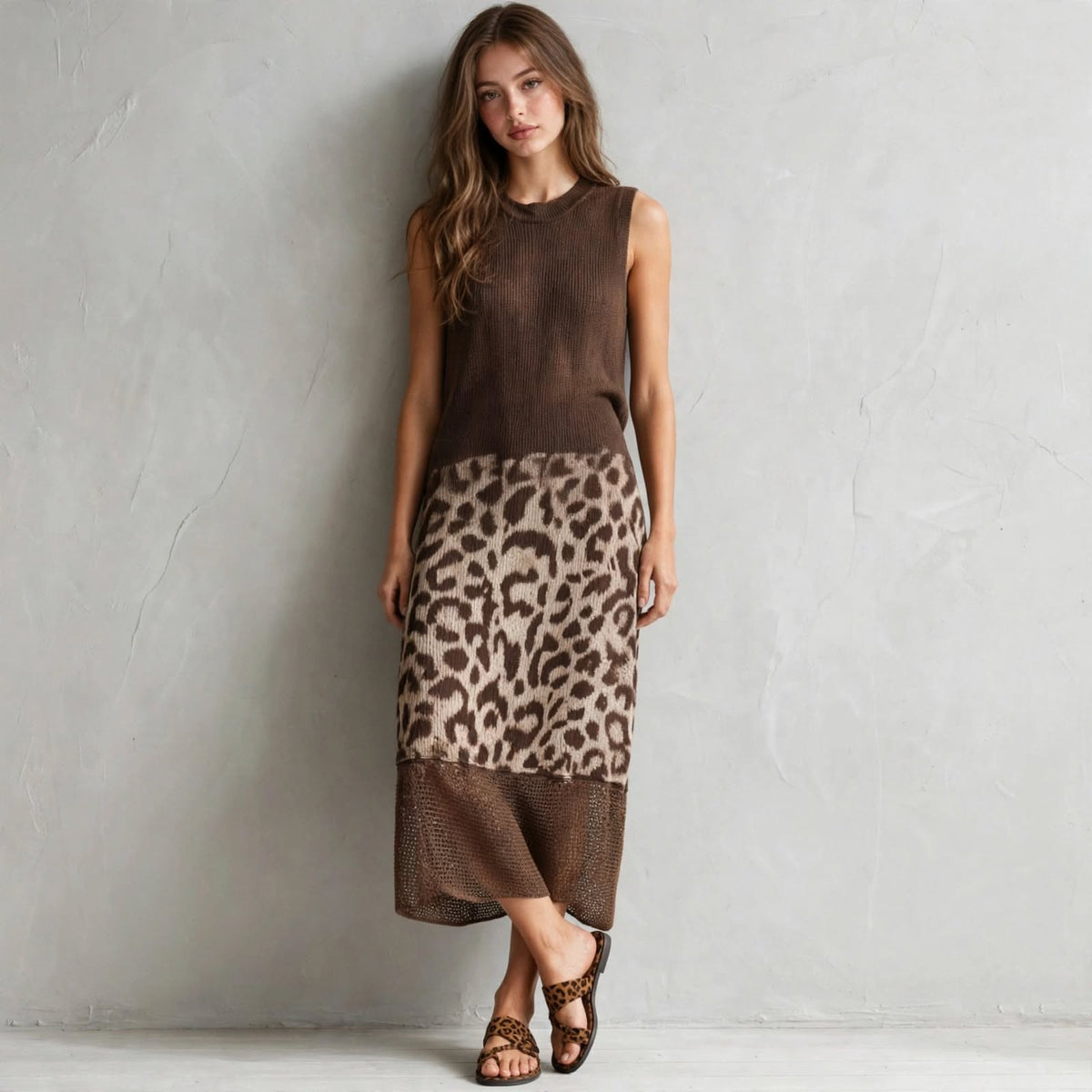 Model posing in a brown sleeveless sweater dress with leopard color-block skirt, legs crossed, brown strappy heels, studio.