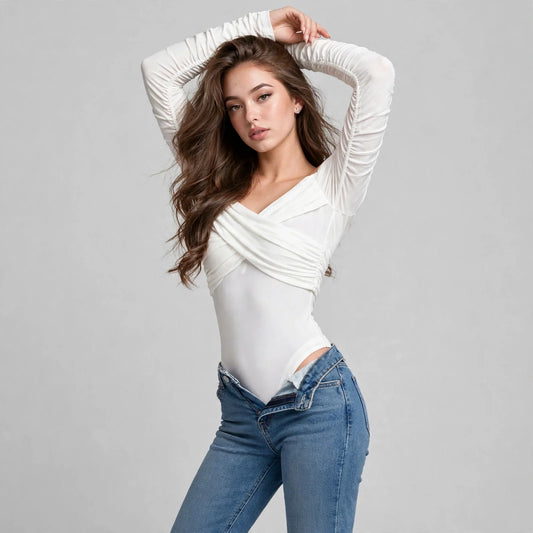 Woman in a white off-shoulder bodysuit and blue jeans, arms raised overhead, full-length pose, gray studio background.