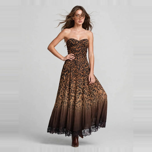 Woman standing with hand on hip in a strapless leopard-print maxi dress with black ombré hem and brown boots, gray studio.