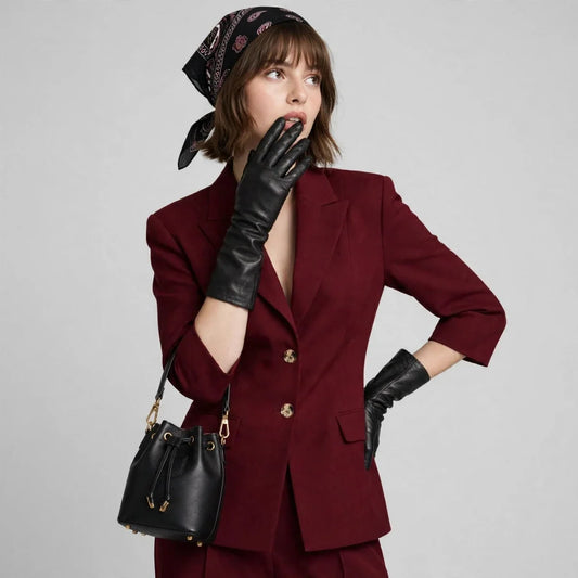 Woman with a finger to her lips wearing a burgundy single-breasted blazer set, black gloves, and a black bucket bag.
