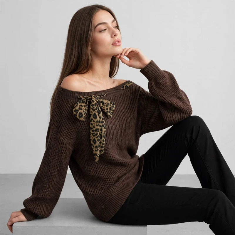 Seated woman in a brown off-shoulder knit sweater with a leopard-print bow at the neckline, black pants, gray studio.