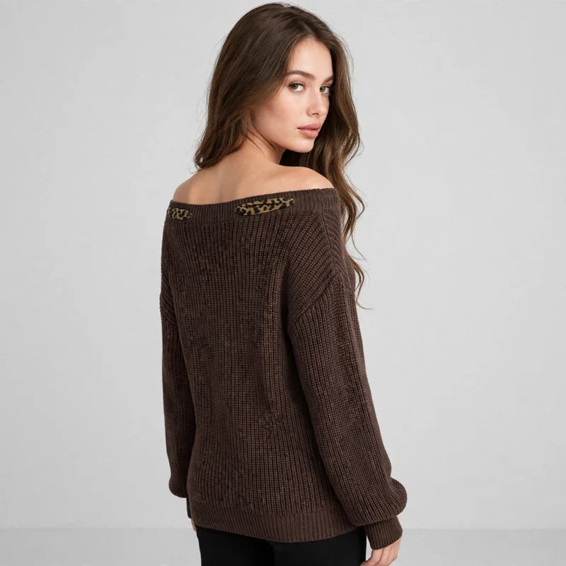 Back view of a brown dropped-shoulder knit sweater with leopard-print trim at the neckline, black pants, gray studio.