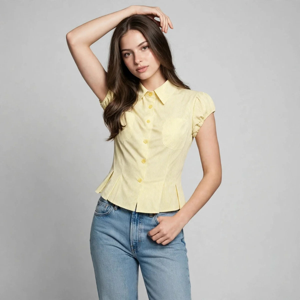 Front view of a woman with one arm raised wearing a yellow pinstripe button-up shirt and blue jeans.