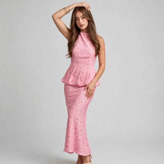 Woman modeling a pink floral halter-neck cami and matching maxi skirt set, hand on head, gray studio background.