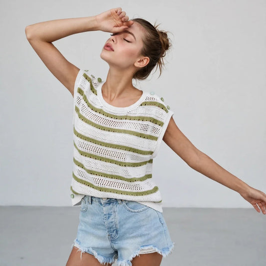 Woman wearing a white and green striped crochet knit top with denim shorts, arm raised, gray studio background.