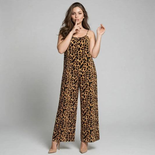Woman with finger to lips in a leopard print wide-leg jumpsuit with thin straps, gray studio background.