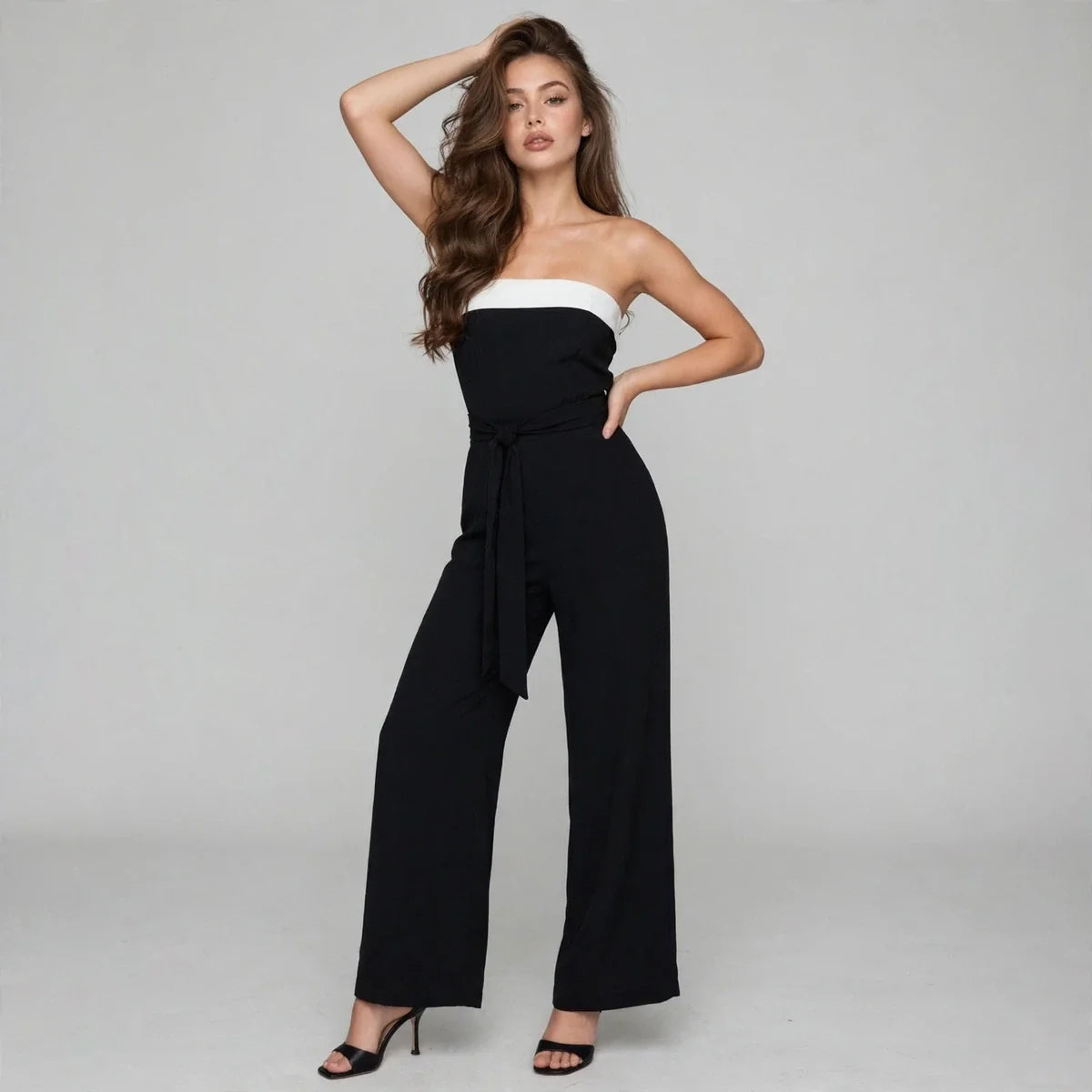 Front view of a black strapless tube jumpsuit with white contrast bust band and tied waist, wide-leg pants, gray studio.