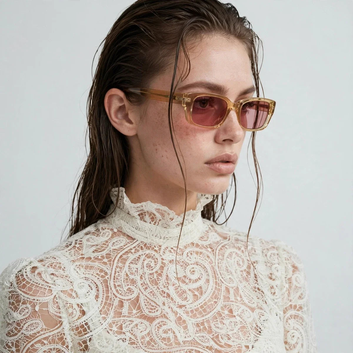 Close-up of a white high-neck lace top with floral pattern worn with sunglasses, light gray studio background.